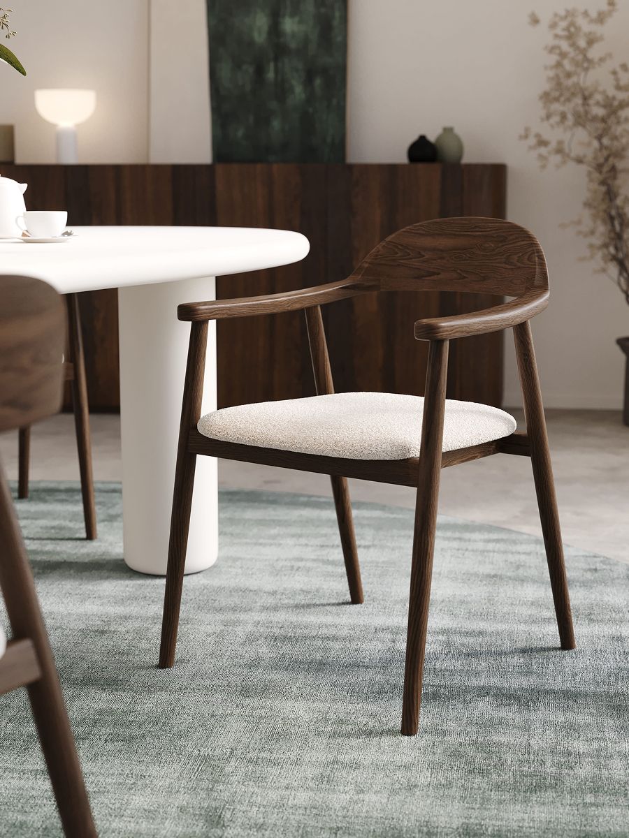 Comino stoel in donker hout met lichtbeige zitting bij witte ronde eettafel op groenblauw vloerkleed.