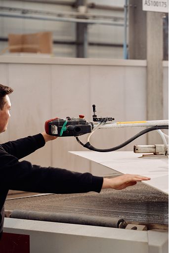 Persoon bedient een grote machine in een atelier, met een wit paneel op de werktafel en slangen/armen van de installatie in beeld.