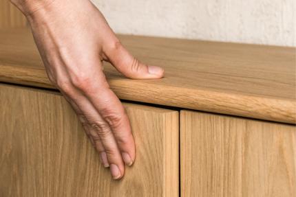 Close-up van een hand op een houten kastdeur, met zichtbaar houtnerf en strakke naad tussen twee fronten.