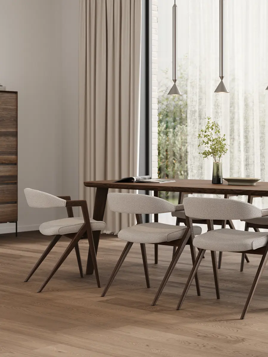 Coin repas lumineux avec une longue table en bois et des chaises rembourrées, sous de fines suspensions près de grandes fenêtres avec voilages.