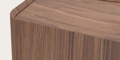 Detail van houten meubel met afgeronde hoek, fijn geribbelde zijkant en warm notenhout blad.