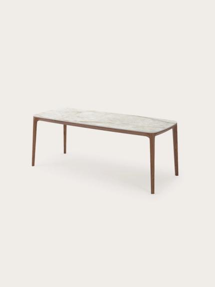 Rechthoekige eettafel met afgeronde hoeken, licht steenlook blad en slanke houten poten.