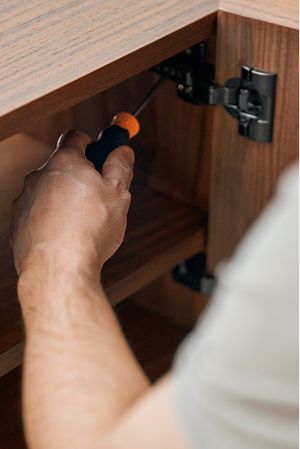 Monteur stelt een scharnier af in een houten kast met een schroevendraaier.
