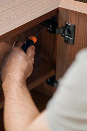 Monteur stelt een scharnier af in een houten kast met een schroevendraaier.