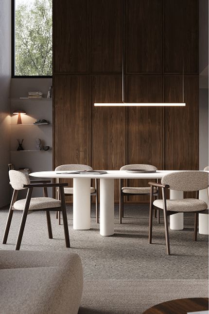 Moderne eethoek met witte ovale eettafel, gestoffeerde stoelen, houten wandkasten en strak hangarmatuur.