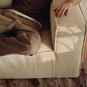 Close-up van de Duomo-zetel in beige stof, met hand op de armleuning en zonlichtschaduw.