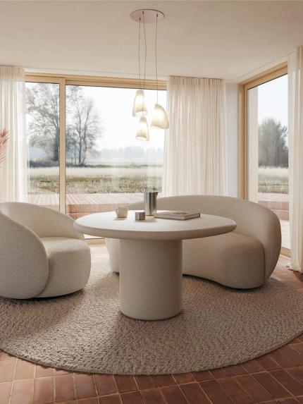 Canapé Ponte beige aux formes arrondies autour d’une table à manger ronde dans un espace lumineux avec grandes fenêtres et vue sur la nature.