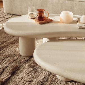 Gros plan de la table Artisano beige clair au plateau arrondi, avec verres et bougie posés dessus.