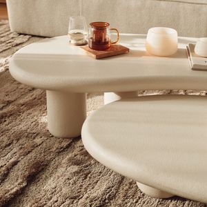 Gros plan de la table Artisano beige clair au plateau arrondi, avec verres et bougie posés dessus.