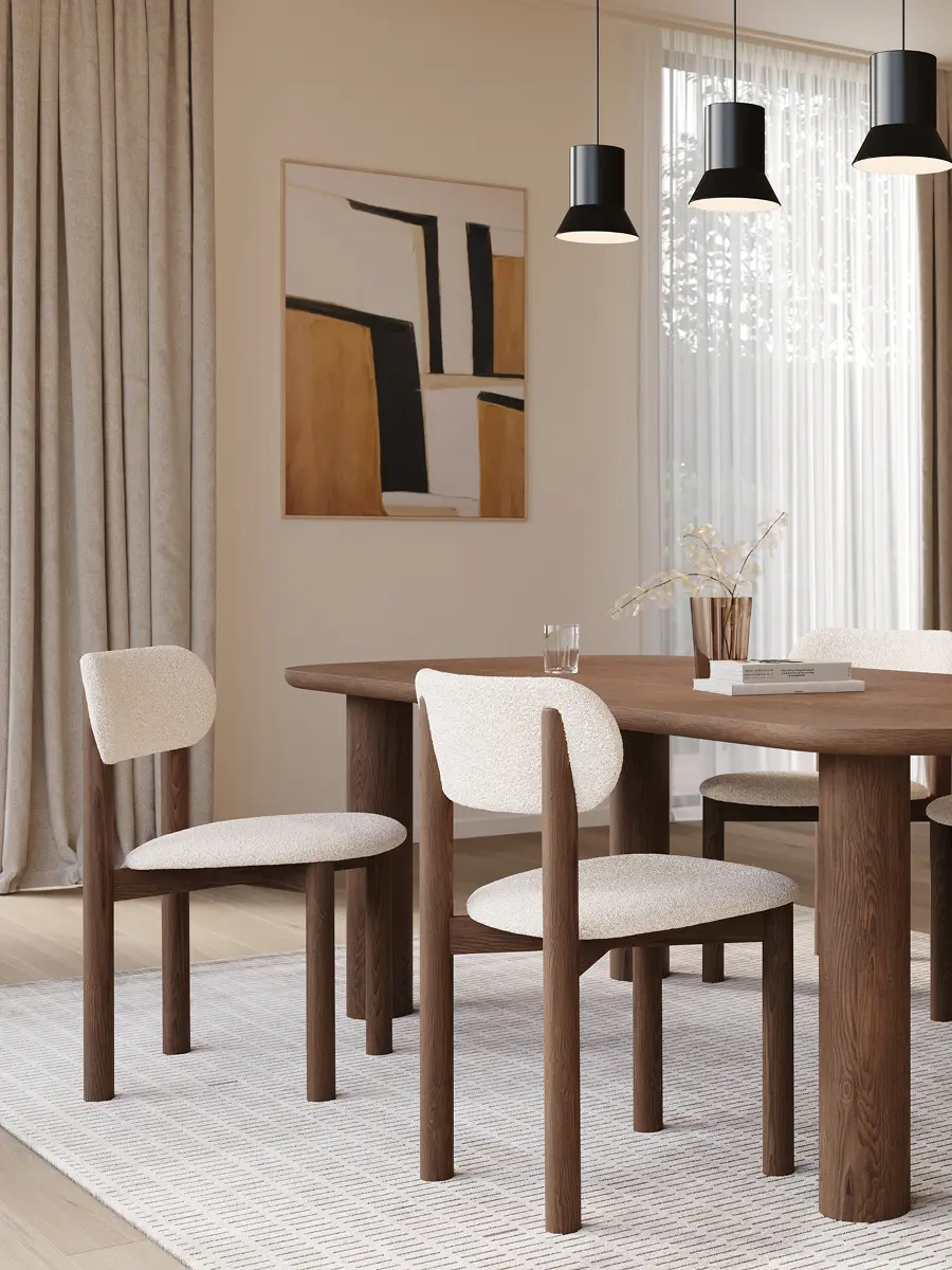 Salle à manger lumineuse avec une longue table en bois et six chaises rembourrées, sous trois suspensions noires près d’une grande fenêtre avec rideaux.