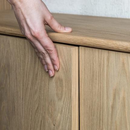 Une main ouvrant délicatement un meuble en bois, mettant en valeur les lignes nettes et le bois chaleureux. Le design souligne la simplicité et le savoir-faire du meuble.