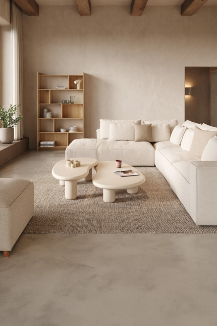 Beige modulaire zetel met kussens in een rustige woonkamer met ronde salontafels, tapijt en houten open kast.