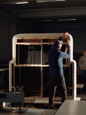 Vakman werkt aan de constructie van een bank, terwijl het frame wordt bekleed met stof in een werkplaats.