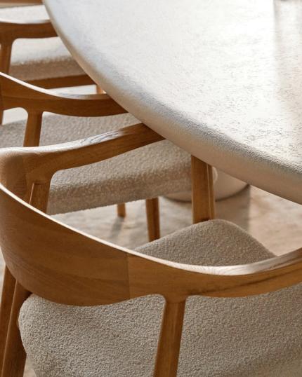 Close-up van houten eetkamerstoelen met beige kussens rond een moderne, ovale eettafel met een gladde, lichte bovenkant.