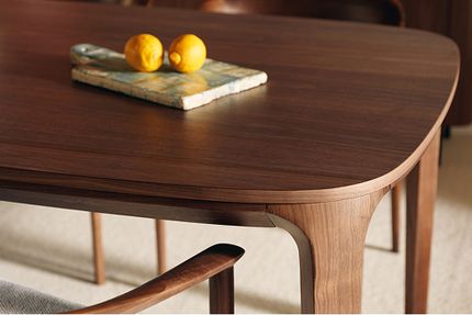 Close-up van een donkerhouten tafel met afgeronde hoek en gebogen pootdetail, met twee citroenen op een marmeren schaaltje.