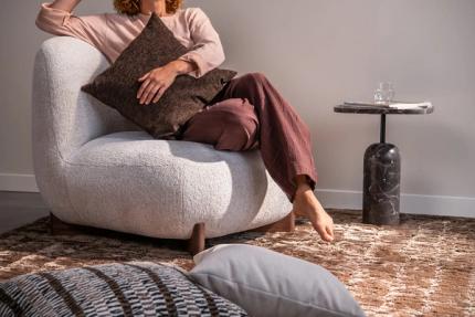 Persoon ontspant in een lichte fauteuil met sierkussen, naast een bijzettafel in donker marmer.