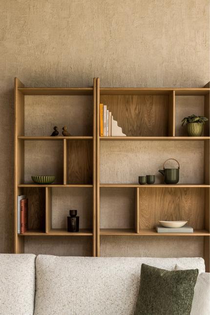 Bibliothèque en bois avec étagères ouvertes et montants arrondis, décorée de livres et de céramiques contre un mur brut.
