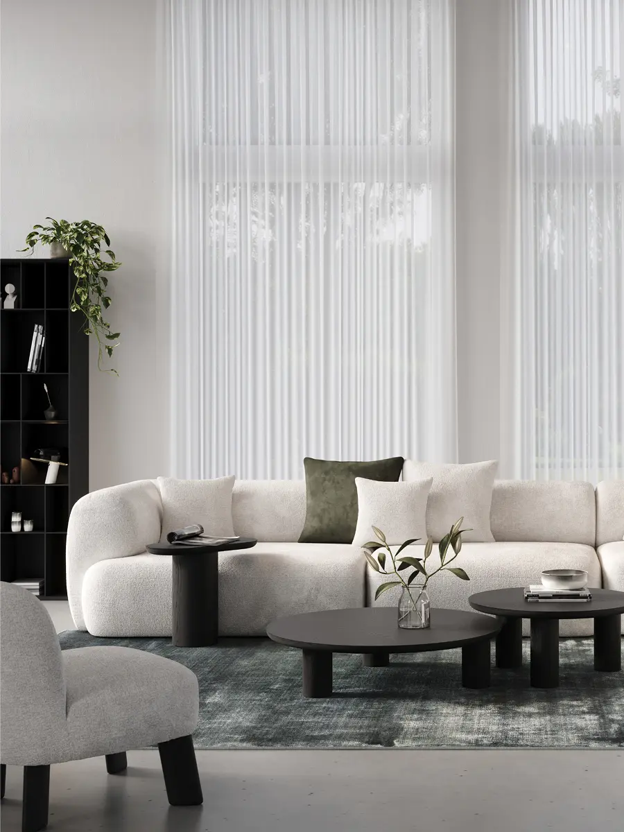 Lichte hoeksofa met wit en olijfgroene kussens, booglamp en ronde zwarte salontafels op een blauwgroen tapijt.