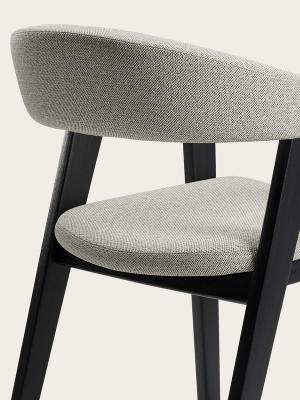 Détail de la chaise Gubbio avec un revêtement en tissu gris clair, un dossier arrondi et des pieds en bois noir.