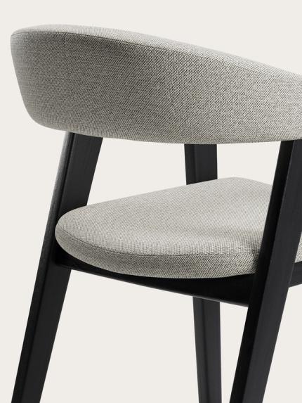 Détail de la chaise Gubbio avec un revêtement en tissu gris clair, un dossier arrondi et des pieds en bois noir.