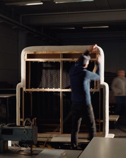 Medewerker plaatst bekleding rond een groot zitmeubelframe in de werkplaats tijdens montage.