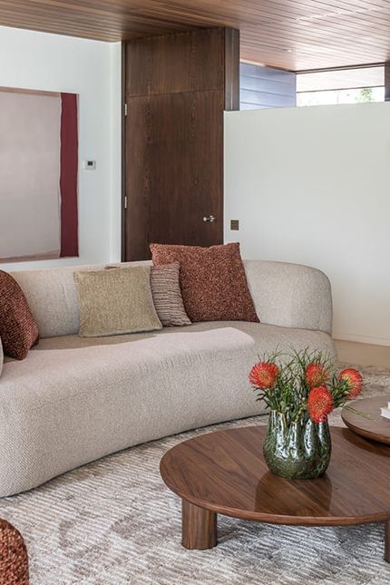 Woonkamer met een lichte gebogen zetel, ronde salontafels in donker hout en een hoge houten kast.