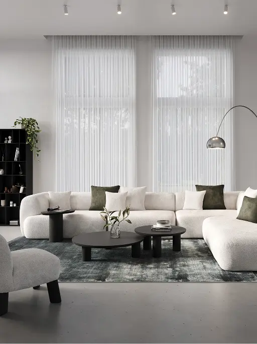 Salon avec canapé modulaire Tortona en tissu gris clair, tables basses rondes noires, tapis vert et grandes fenêtres avec rideaux légers.