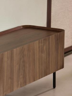 Detailbeeld van een moderne houten tv-kast met verticale latjesstructuur, afgeronde hoeken en slanke zwarte poten.