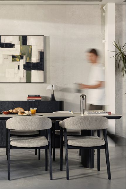 Zwarte ovale eettafel met zes grijze stoelen en ontbijt, met laag dressoir en abstract kunstwerk.