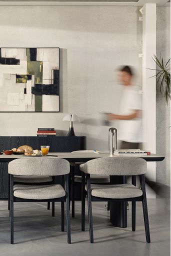 Zwarte ovale eettafel met zes grijze stoelen en ontbijt, met laag dressoir en abstract kunstwerk.