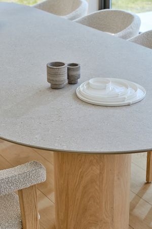 Detailbeeld van een eettafel met een licht, steenachtig blad met afgeronde hoeken en een brede cilindervormige houten poot, gedecoreerd met keramisch servies.