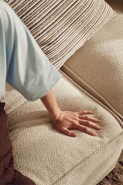 Une main reposant sur le tissu doux et texturé d'un canapé beige dans un espace de vie moderne.
