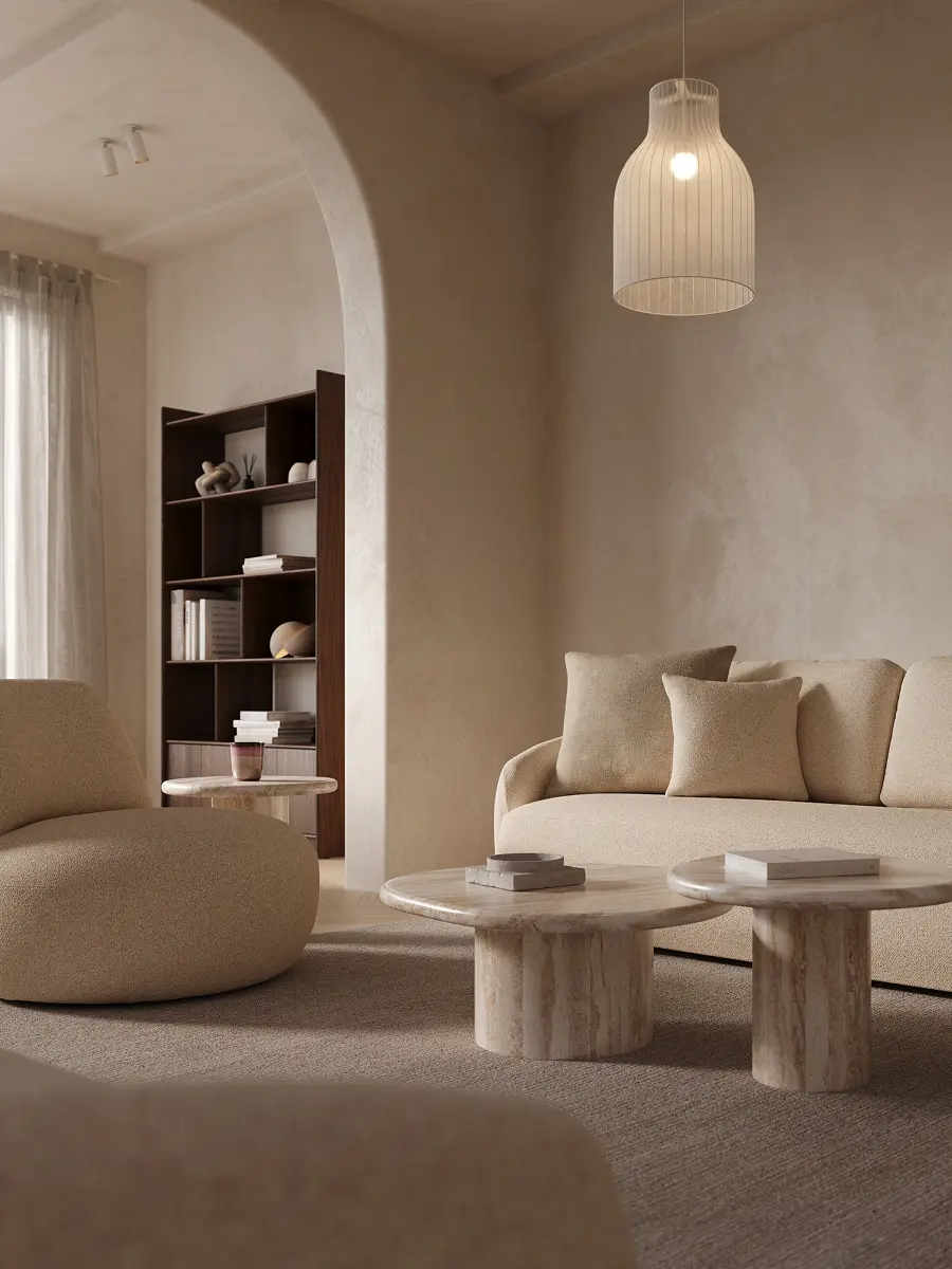 Rustige zithoek met beige sofa en ronde marmeren salontafels op een tapijt, onder een hanglamp, met een boogdoorgang en boekenkast op de achtergrond.