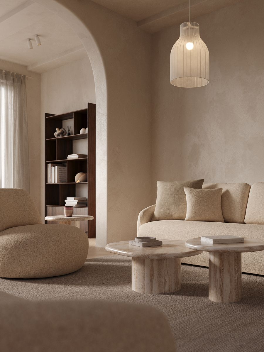 Rustige zithoek met beige sofa en ronde marmeren salontafels op een tapijt, onder een hanglamp, met een boogdoorgang en boekenkast op de achtergrond.