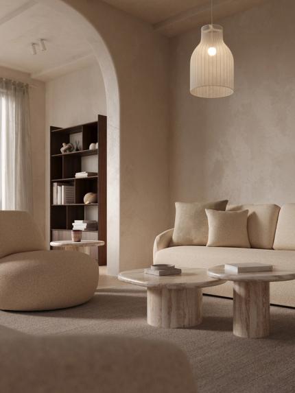 Coin salon apaisant avec canapé beige et tables basses rondes en marbre sur un tapis, sous une suspension, avec une arche et une bibliothèque à l’arrière-plan.