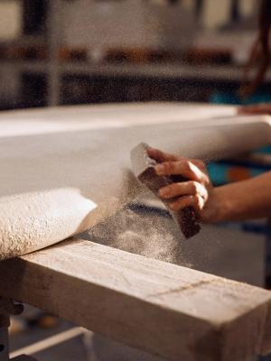 Close-up van een hand die een houten oppervlak schuurt, met stofdeeltjes die in de werkplaats zweven, wat vakmanschap toont.