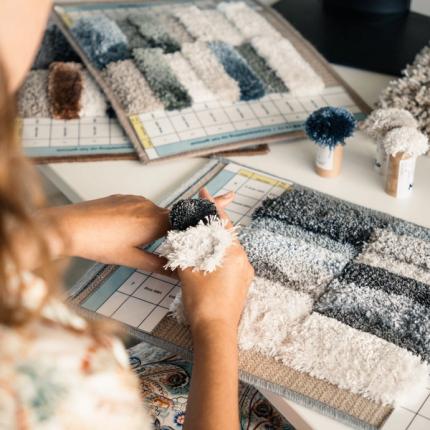 Textielontwerpster vergelijkt verschillende kleuren, structuren en garenstalen bij het ontwerpen van een hoogpolig tapijt.