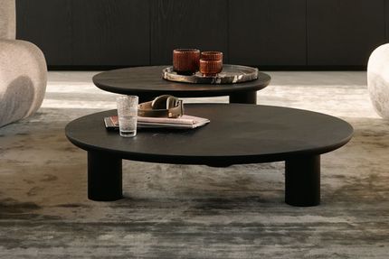 Close-up van twee lage, ronde zwarte salontafels met dikke poten, gestyled met glazen en kaarsen op een marmeren dienblad.