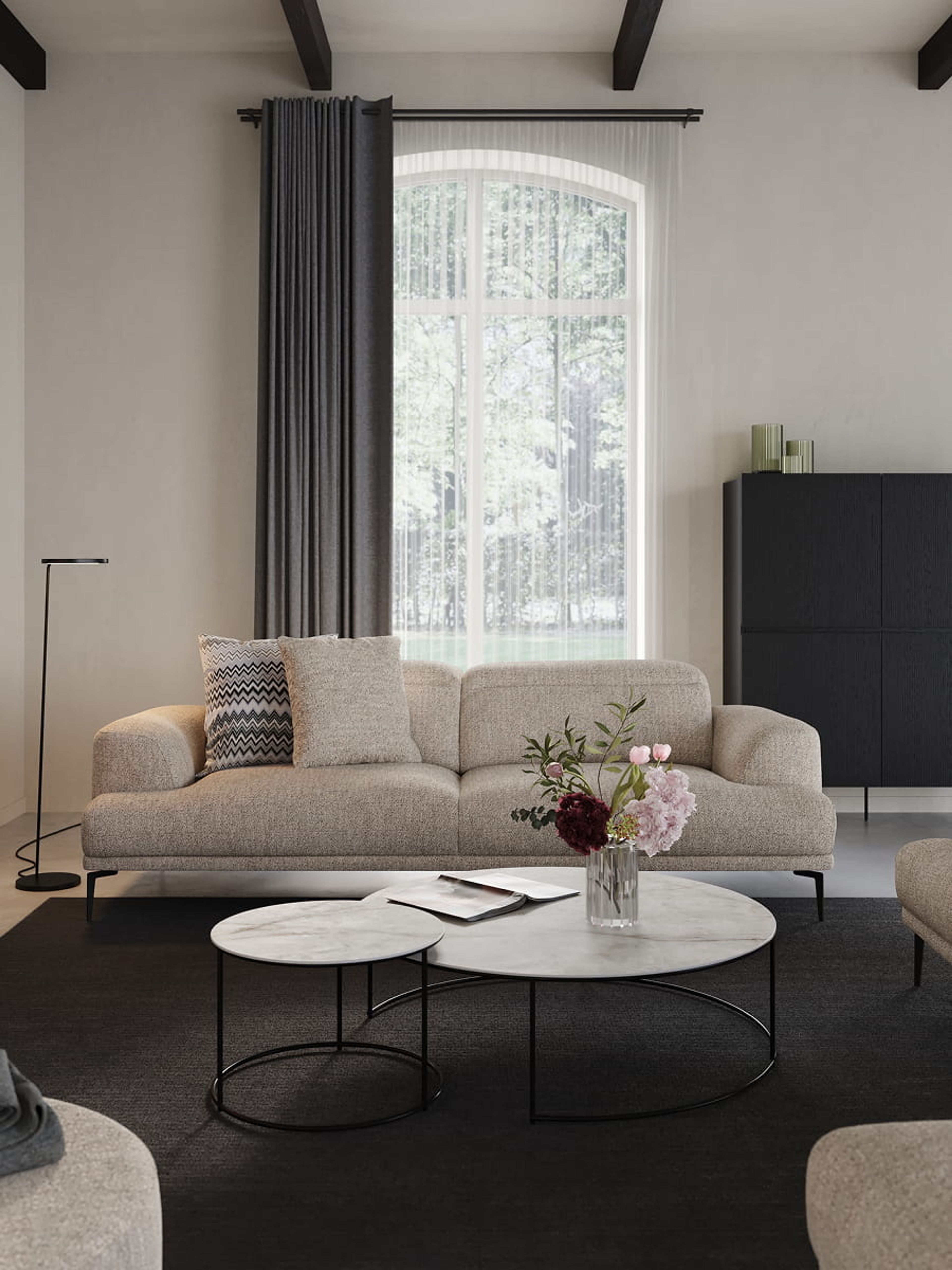 Grijze zetel Funchal in lichte woonkamer met ronde marmeren salontafels, zwarte kast, grote ramen en een vaas met bloemen.