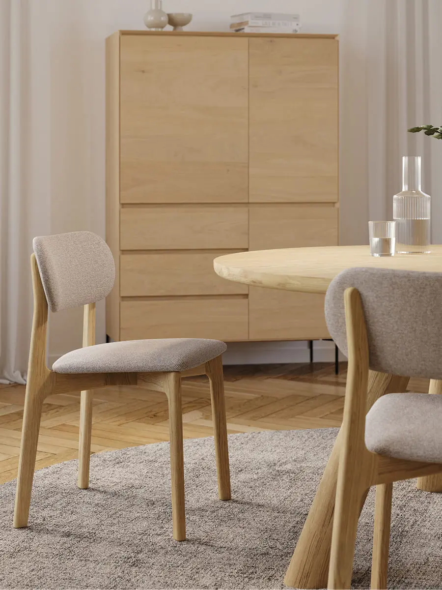 Salle à manger lumineuse avec table ronde en bois et chaises rembourrées, avec un meuble en bois à l’arrière-plan.
