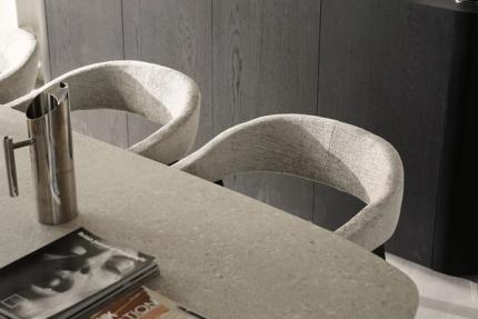 Cuisine moderne avec une table à manger en béton et des chaises rembourrées à dossiers ronds, accompagnées d'une élégante carafe en métal et de magazines.