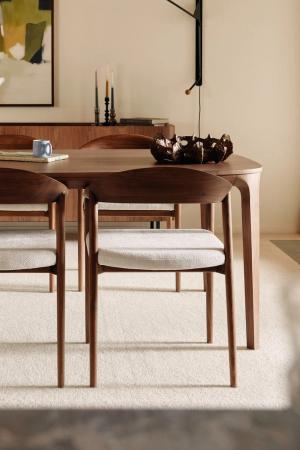 Houten eetkamerstoelen met lichte gestoffeerde zitting rond een afgeronde houten eettafel in een warme eetkamer.