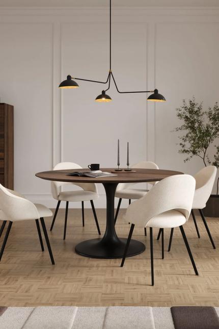 Compacte eetruimte met ronde houten tafel op zwarte voet en lichte stoelen, in een rustige setting met parketvloer en kamerplant.