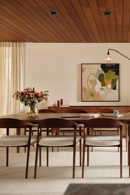 Moderne eetkamer met een houten tafel, beige gestoffeerde stoelen, een vaas met bloemen op de tafel en een abstract kunstwerk aan de muur.