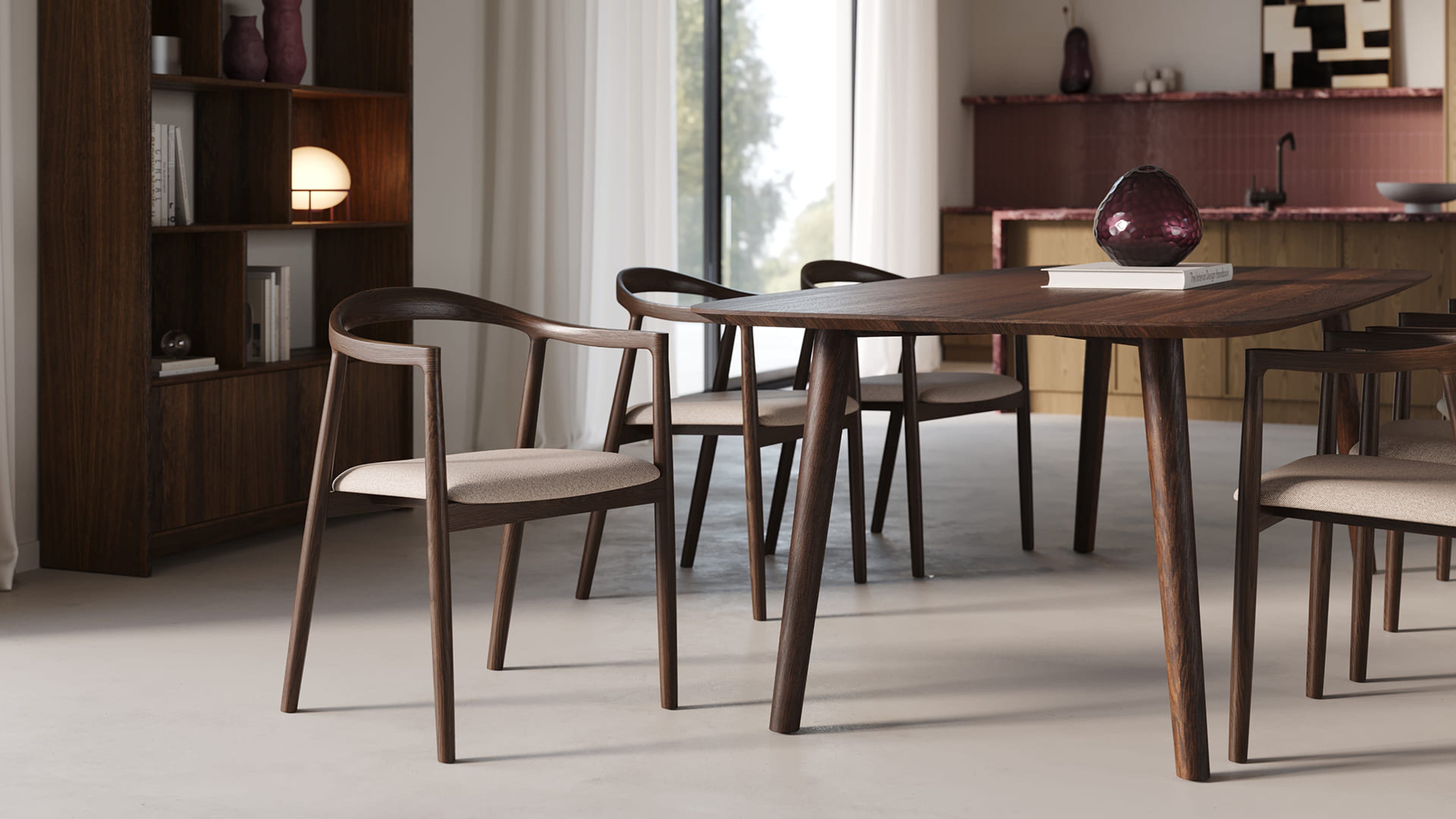 Donkere houten eettafel met vier stoelen in lichte stof, in rustige eetkamer met boekenkast en keuken op achtergrond.