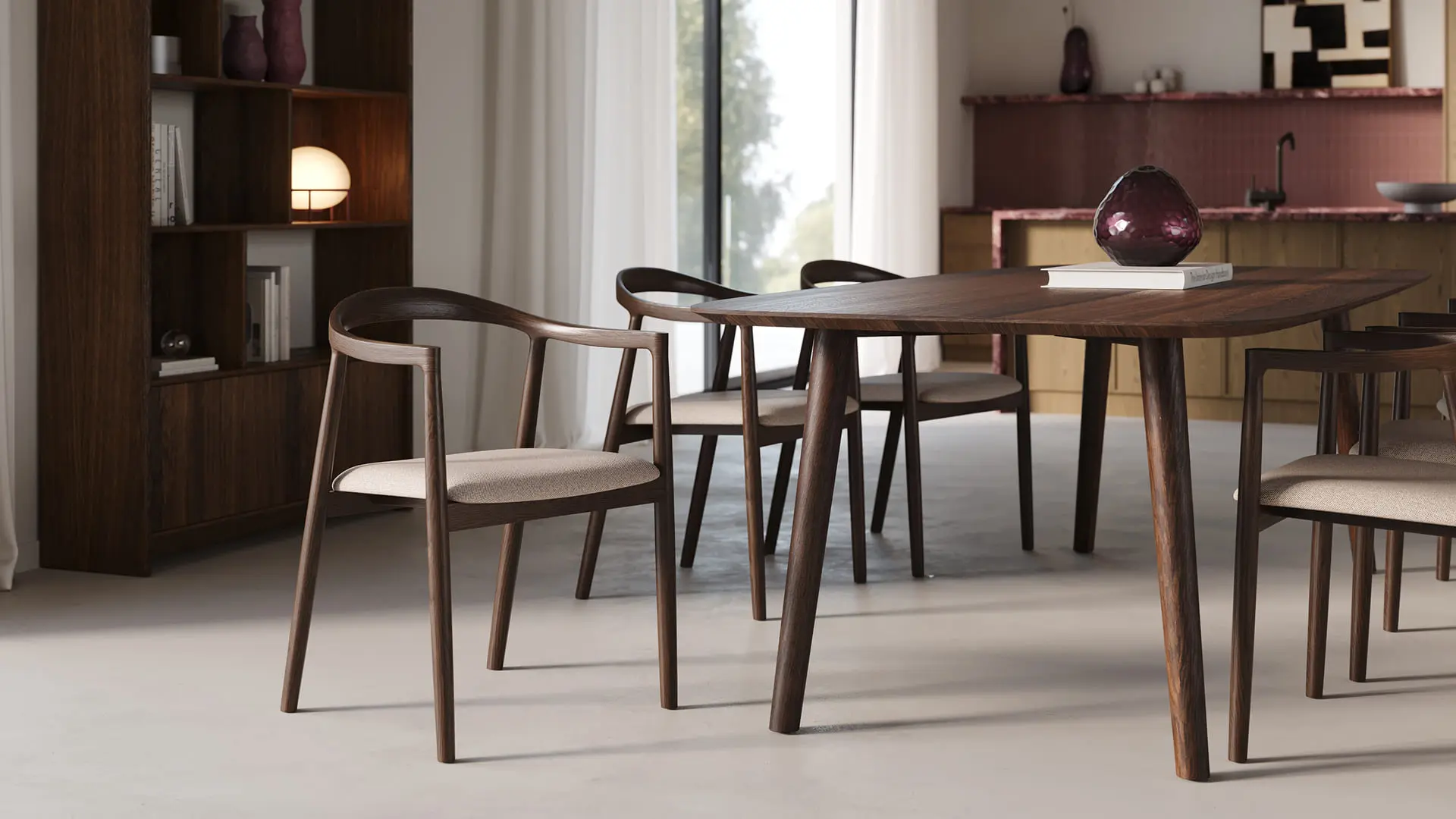 Table à manger en bois foncé avec quatre chaises en tissu clair, dans une salle à manger calme avec bibliothèque et cuisine en fond.