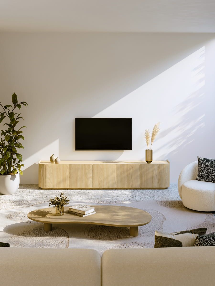 Salon lumineux avec meuble TV bas en bois sous une télévision murale, table basse ronde et fauteuil blanc, avec des plantes et la lumière douce du soleil.