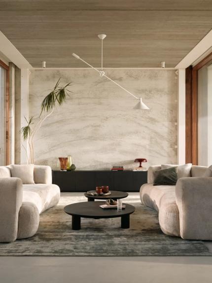 Deux canapés arrondis en tissu clair se font face dans un salon moderne, avec grandes baies vitrées, table basse noire et tapis doux.