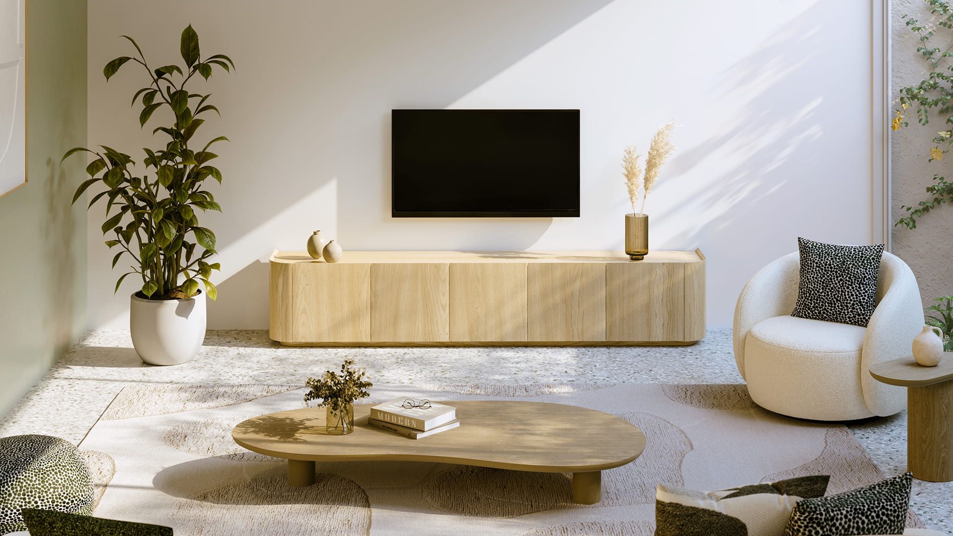 Salon lumineux avec meuble TV bas en bois sous une télévision murale, table basse ronde et fauteuil blanc, avec des plantes et la lumière douce du soleil.