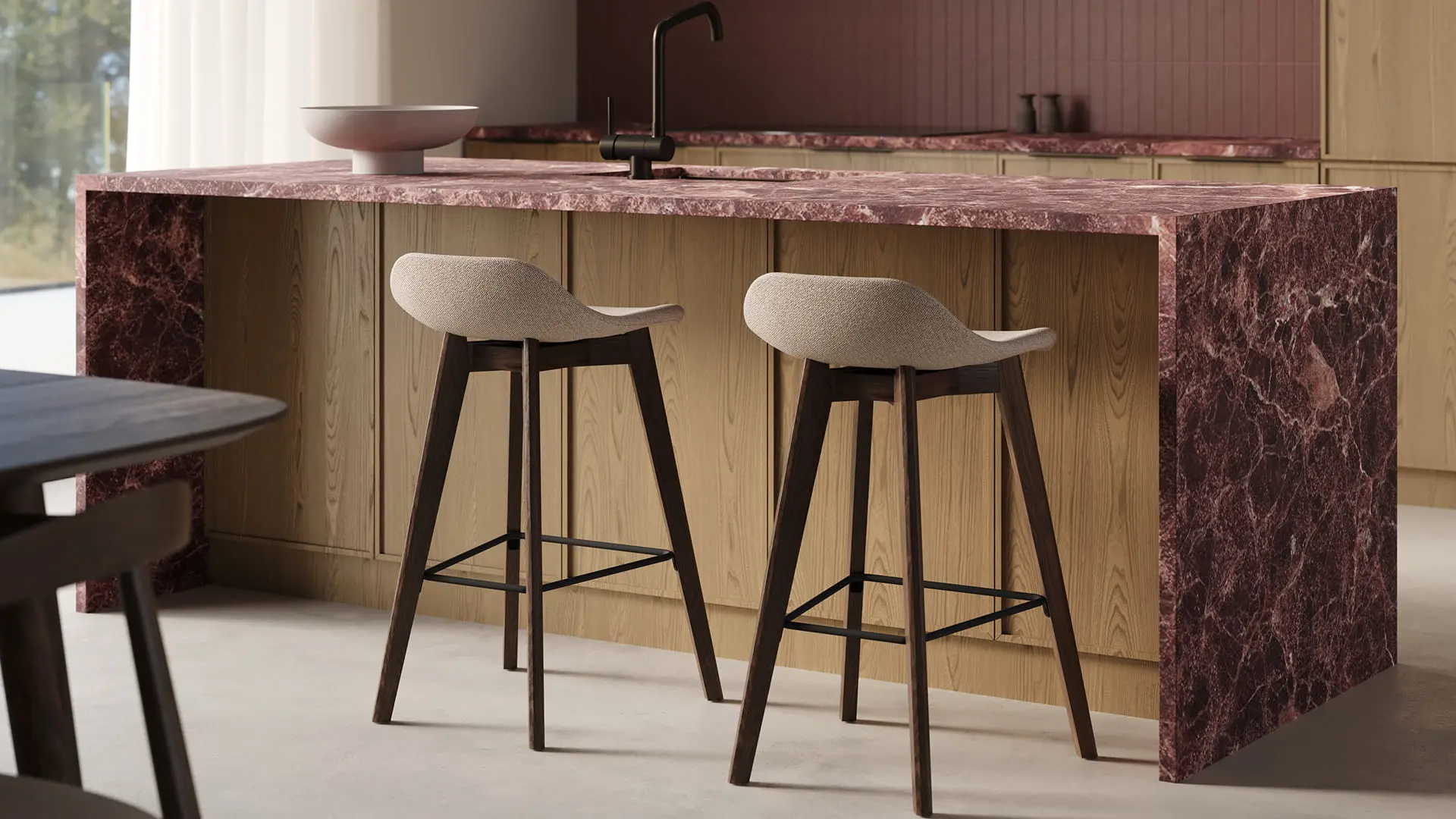 Deux tabourets de bar Vasco, assise claire et pieds foncés, devant un îlot en bois avec plan de travail en marbre rouge.